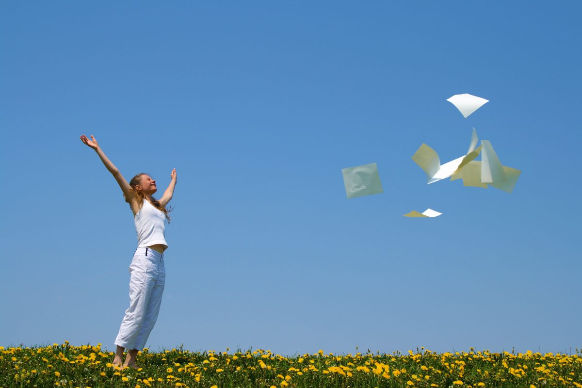 Glückliche Frau auf einem Feld, die Papier in die Luft wirft vor blauem HImmel